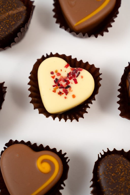 Heart-shaped red tin box filled with seven assorted handmade heart chocolates, including dark, milk, and white chocolate pralines.