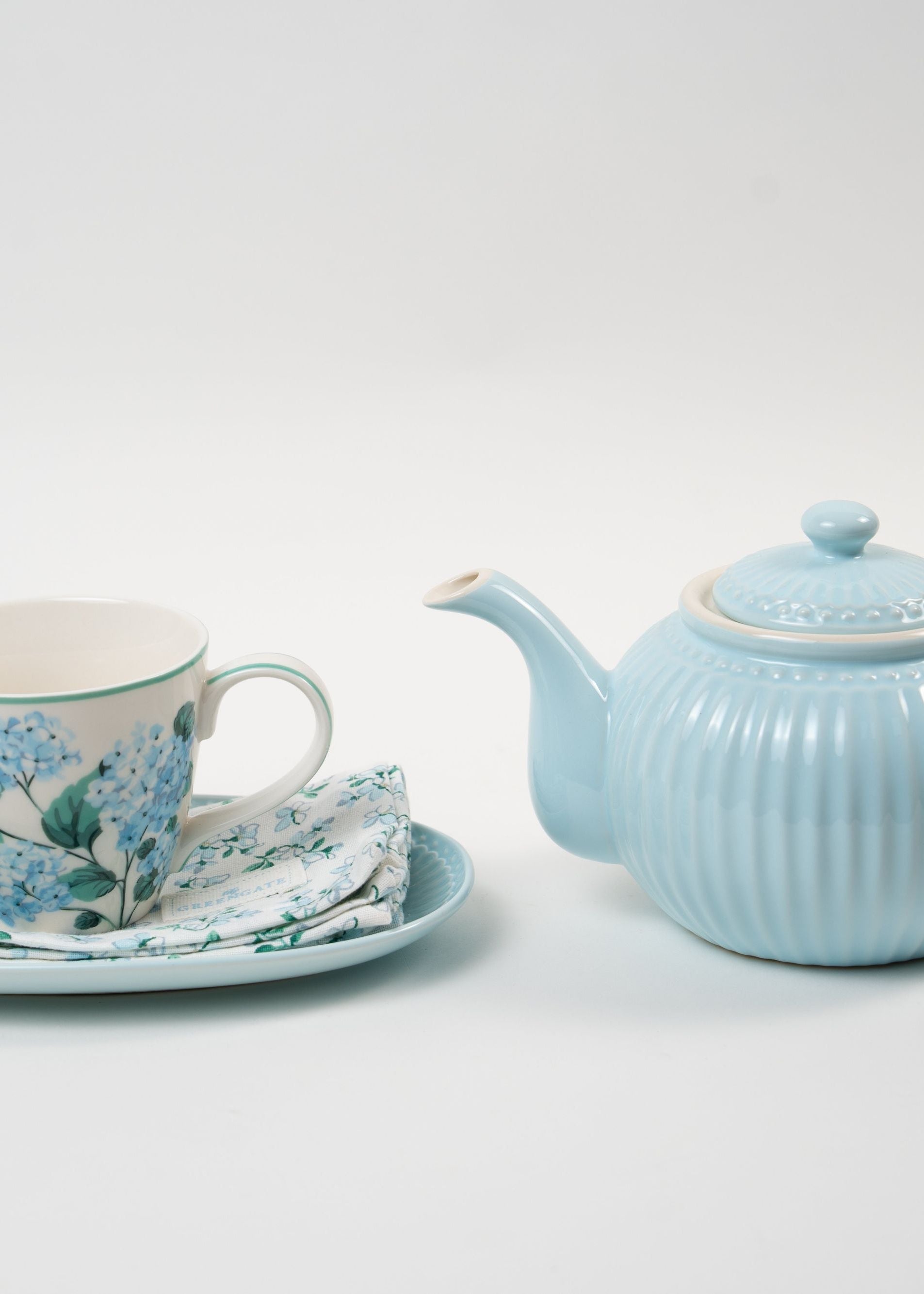 Service à thé raffiné composé d’une théière en céramique bleu pastel nervurée, accompagné d’une tasse fleurie avec soucoupe et serviette assortie. Une harmonie douce et élégante pour sublimer vos moments de dégustation.