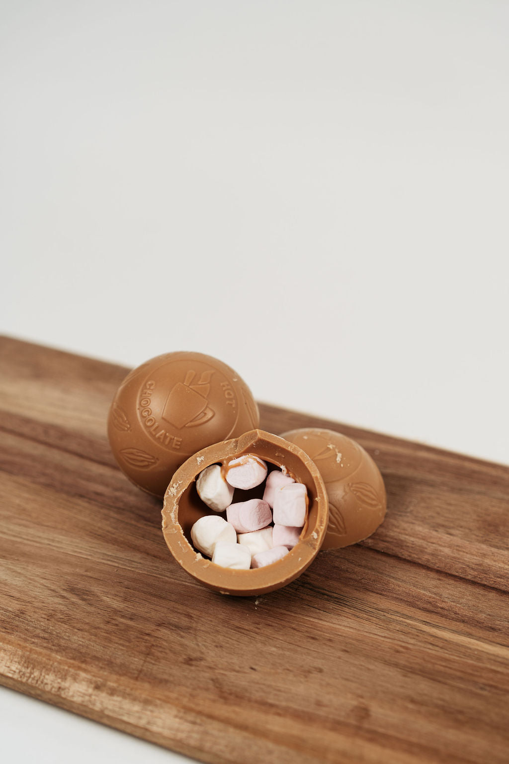 Bombe de chocolat chaud caramel ouverte avec mini marshmallows à l’intérieur sur planche en bois