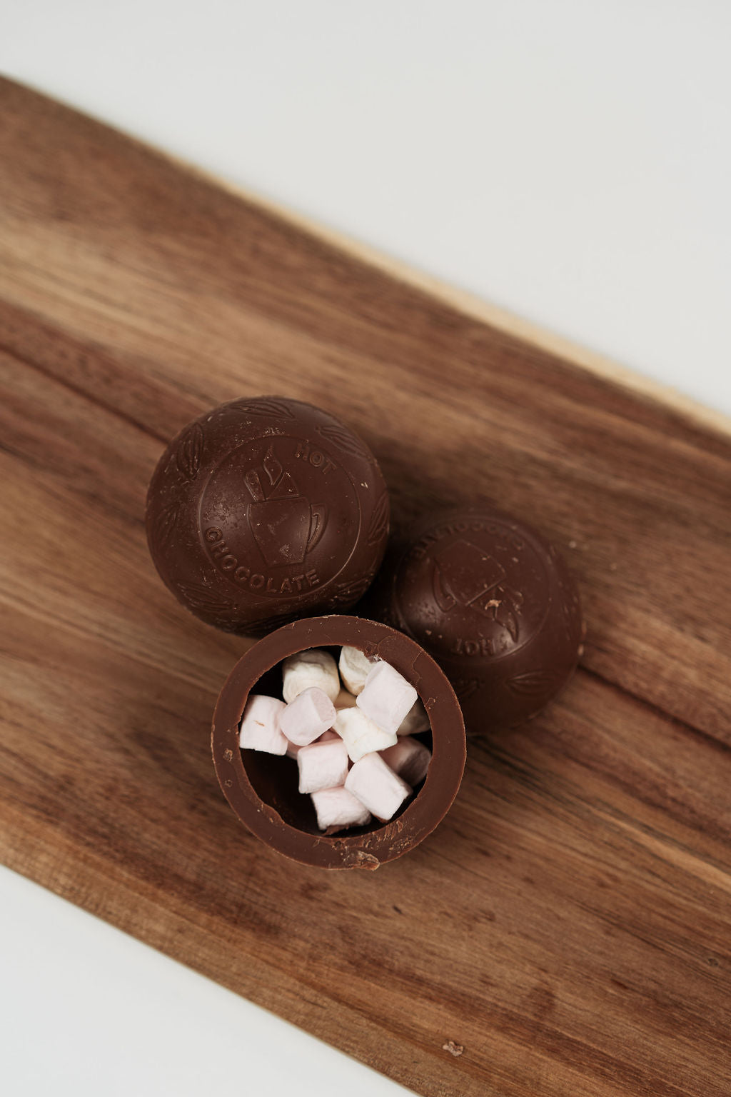 Bombe de chocolat chaud au lait ouverte avec mini marshmallows à l’intérieur sur planche en bois