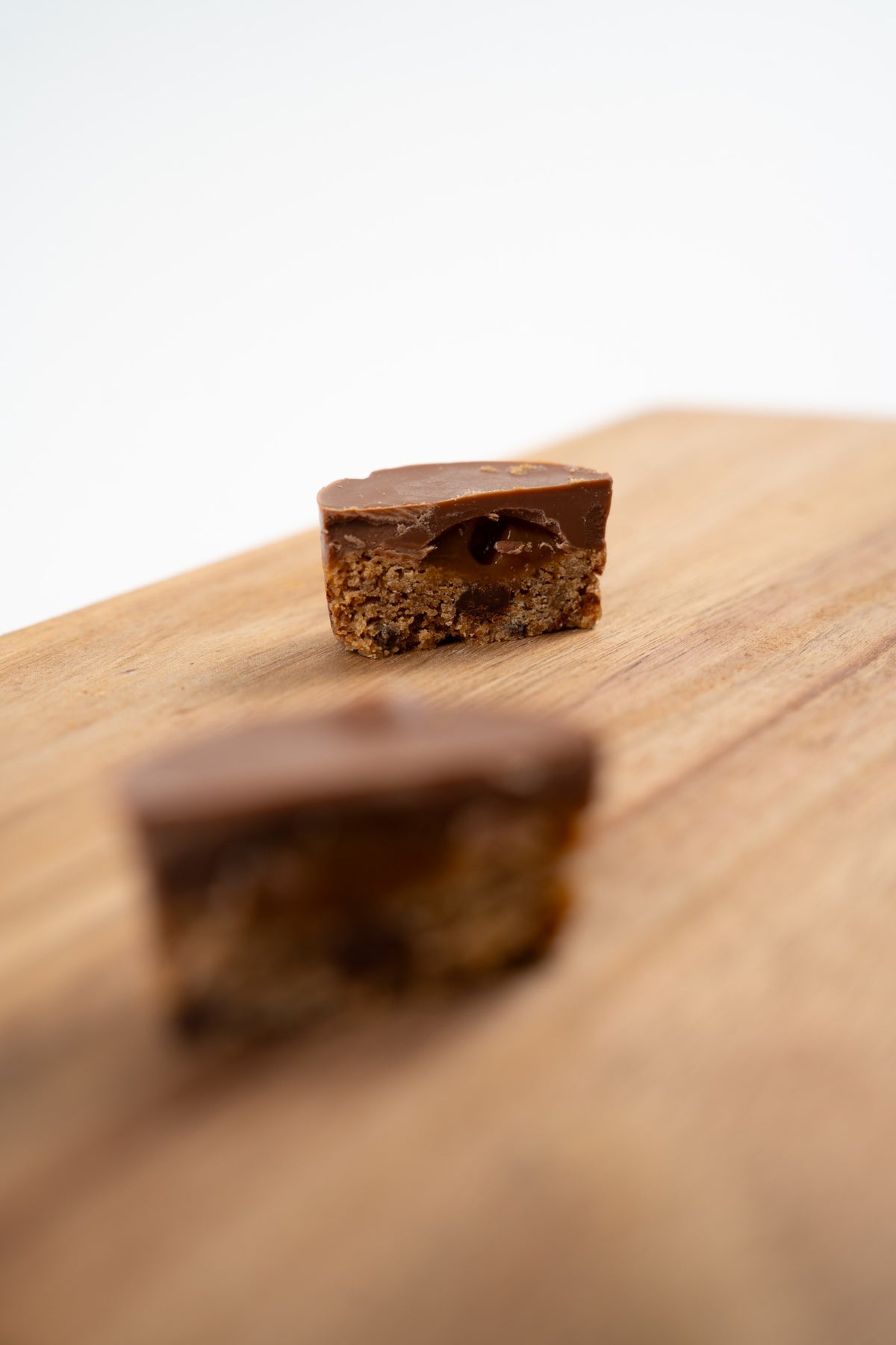 Gros plan d'une bouchée au chocolat au lait coupée en deux, montrant un cœur brun brillant et une base biscuitée, avec une seconde bouchée floue en arrière-plan.