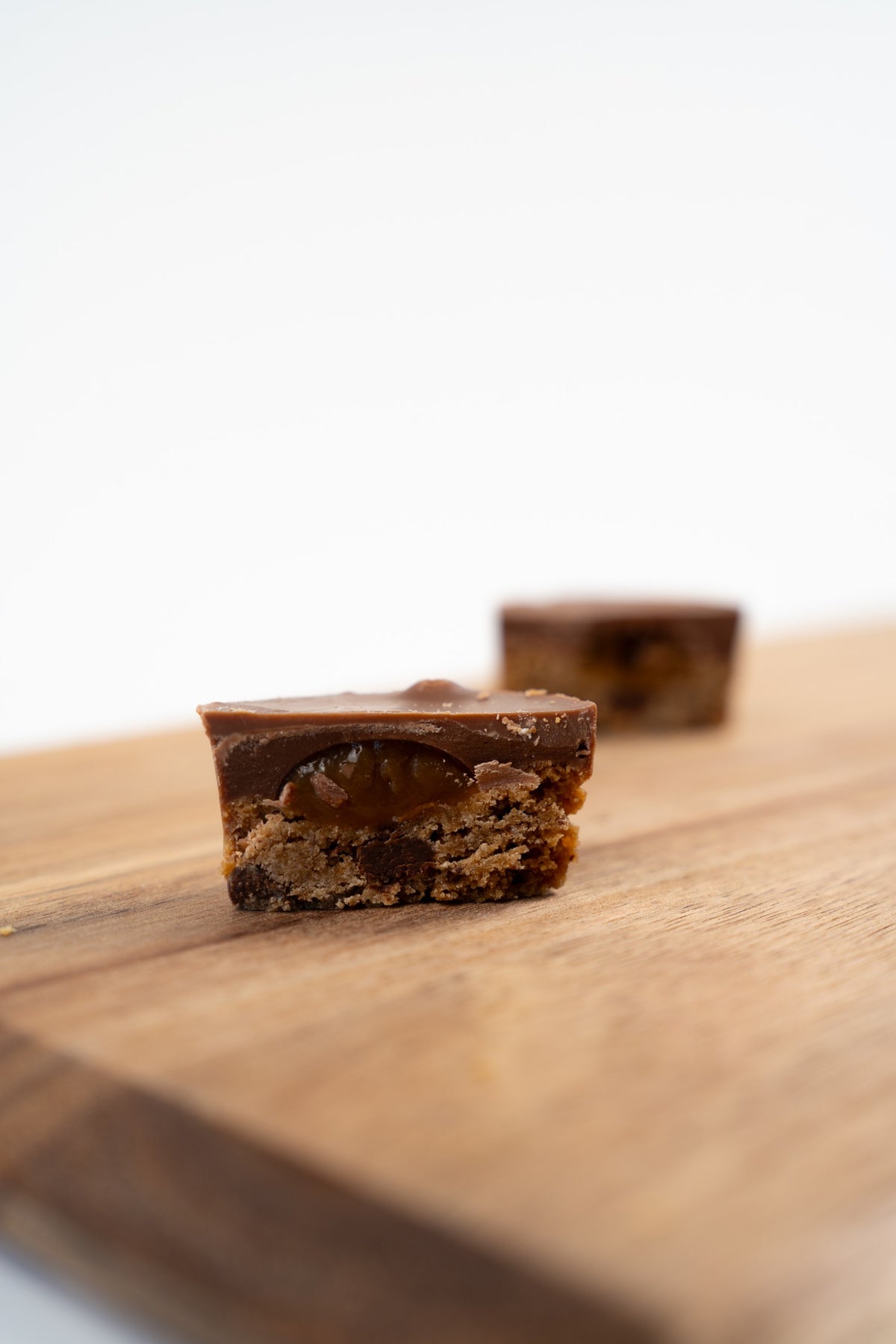 Bouchée au chocolat au lait coupée en deux, révélant un cœur brun fondant et une base biscuitée, sur une planche en bois, avec une seconde bouchée floue au premier plan.