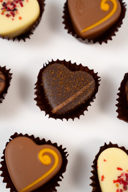 Heart-shaped red tin box filled with seven assorted handmade heart chocolates, including dark, milk, and white chocolate pralines.
