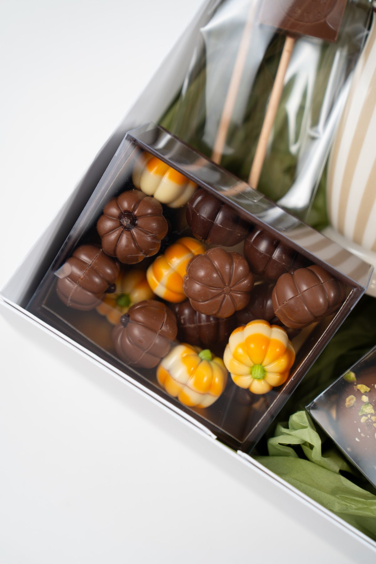 Assortment of Belgian pumpkin-shaped chocolates in milk, dark and white chocolate, presented in a clear box inside an autumn gift box.