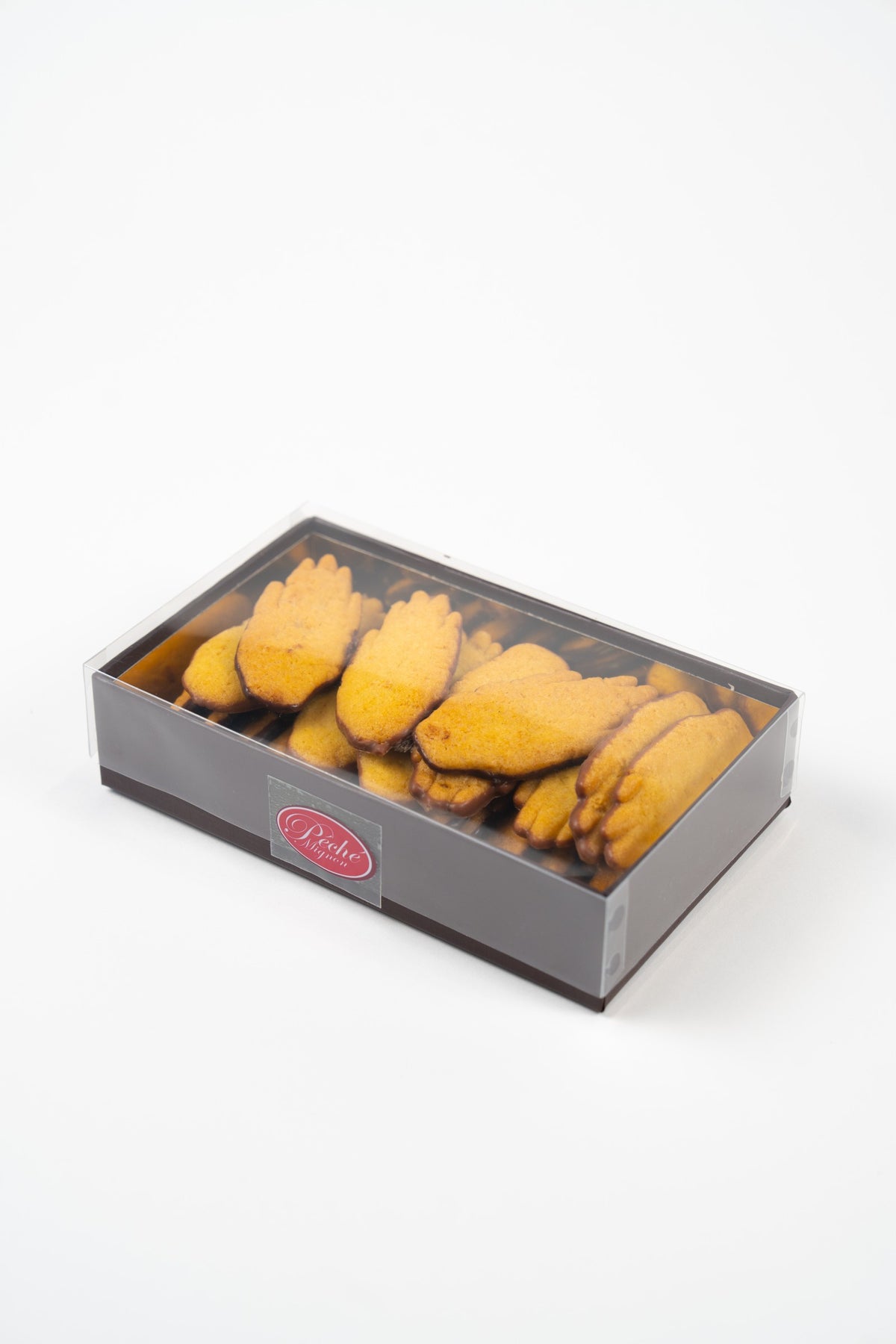 Estuche Péché Mignon con tapa transparente y galletas doradas con forma de mano, parcialmente recubiertas de chocolate, fotografiado en perspectiva sobre fondo blanco.