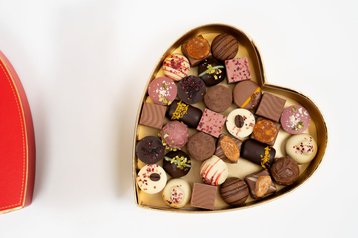 Open heart-shaped box of assorted chocolates with its red lid alongside