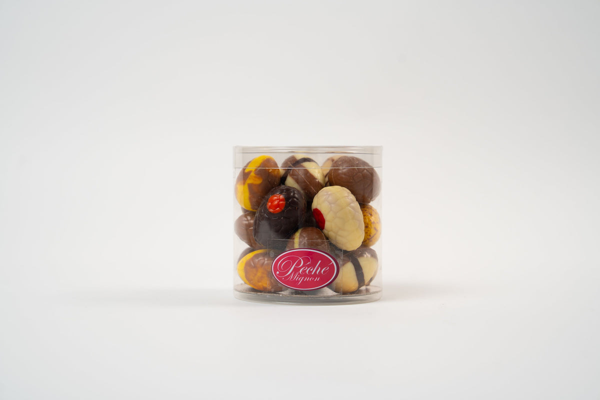 Coffret cadeau transparent d'œufs gourmands en chocolat Péché Mignon, assortiment de chocolats fourrés artisanaux pour offrir lors des fêtes de Pâques.
