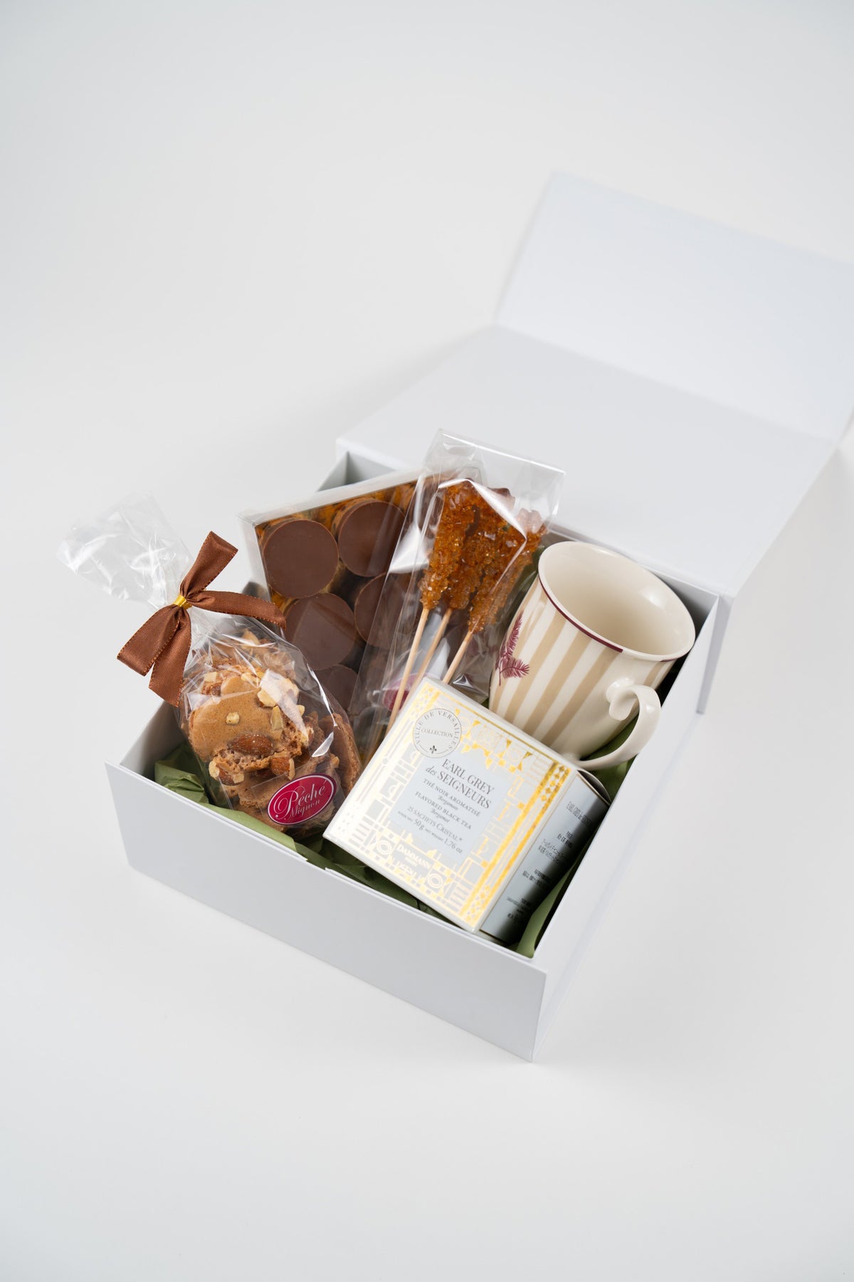 Overhead view of an autumn tea-time gift box with chocolates, almond meringues, Earl Grey tea, rock sugar sticks and a ceramic mug.