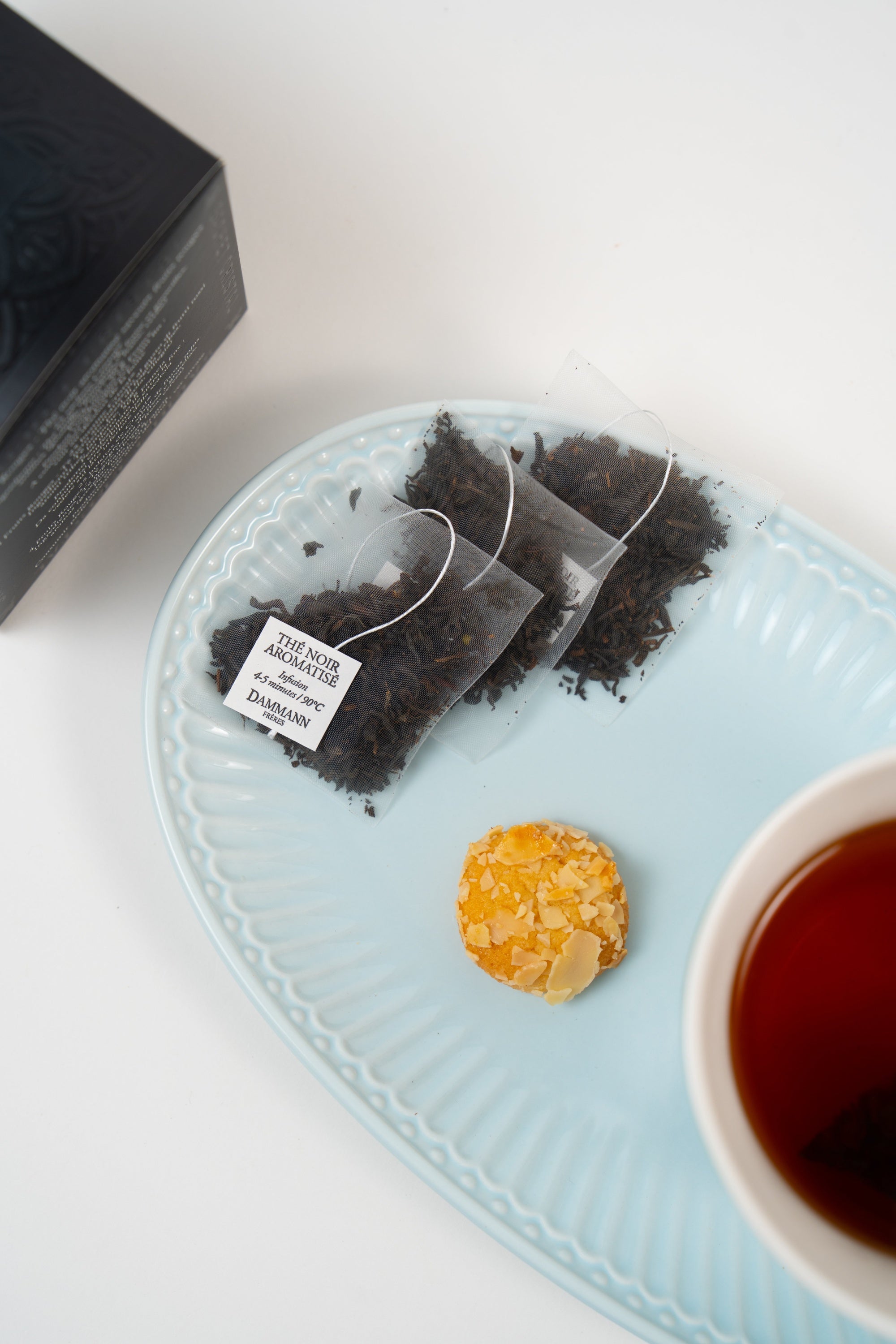 Dammann Frères red berries black tea sachets served with brewed black tea and delicate biscuit on pastel blue porcelain