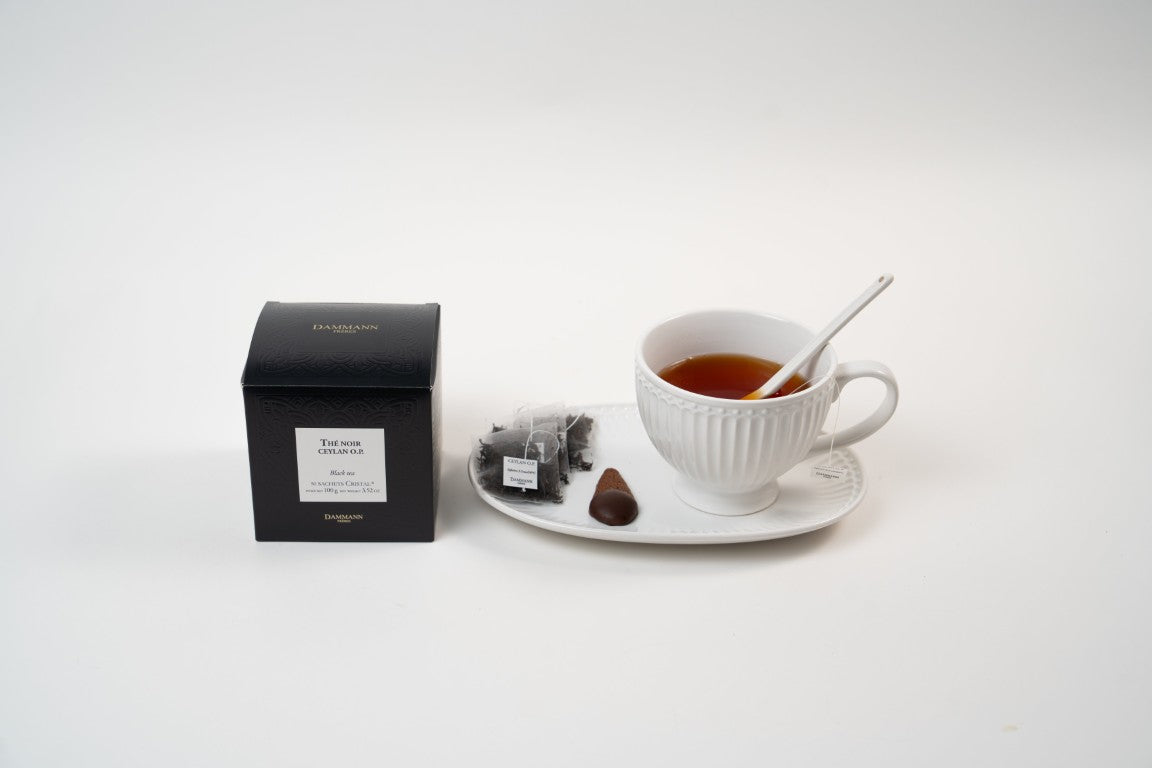 Dammann Frères Ceylan O.P. black tea with teacup, tea sachets and chocolate biscuit on plate.