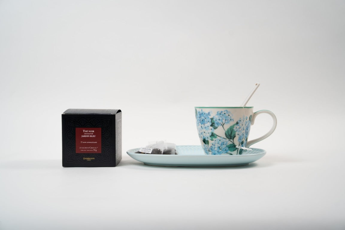 Cup of Jardin Bleu black tea with Dammann Frères tea box, tea sachets and biscuit.