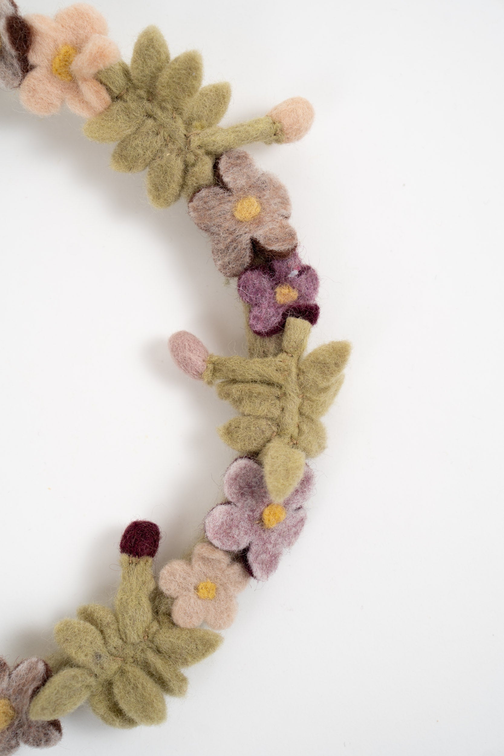 Detailed view of a handmade felt floral wreath with pastel flowers, green leaves and wool buds