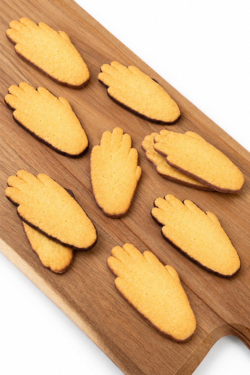 Manos de Amberes, galletas doradas con forma de mano y una fina capa de chocolate con leche en la base, dispuestas sobre una tabla de madera.