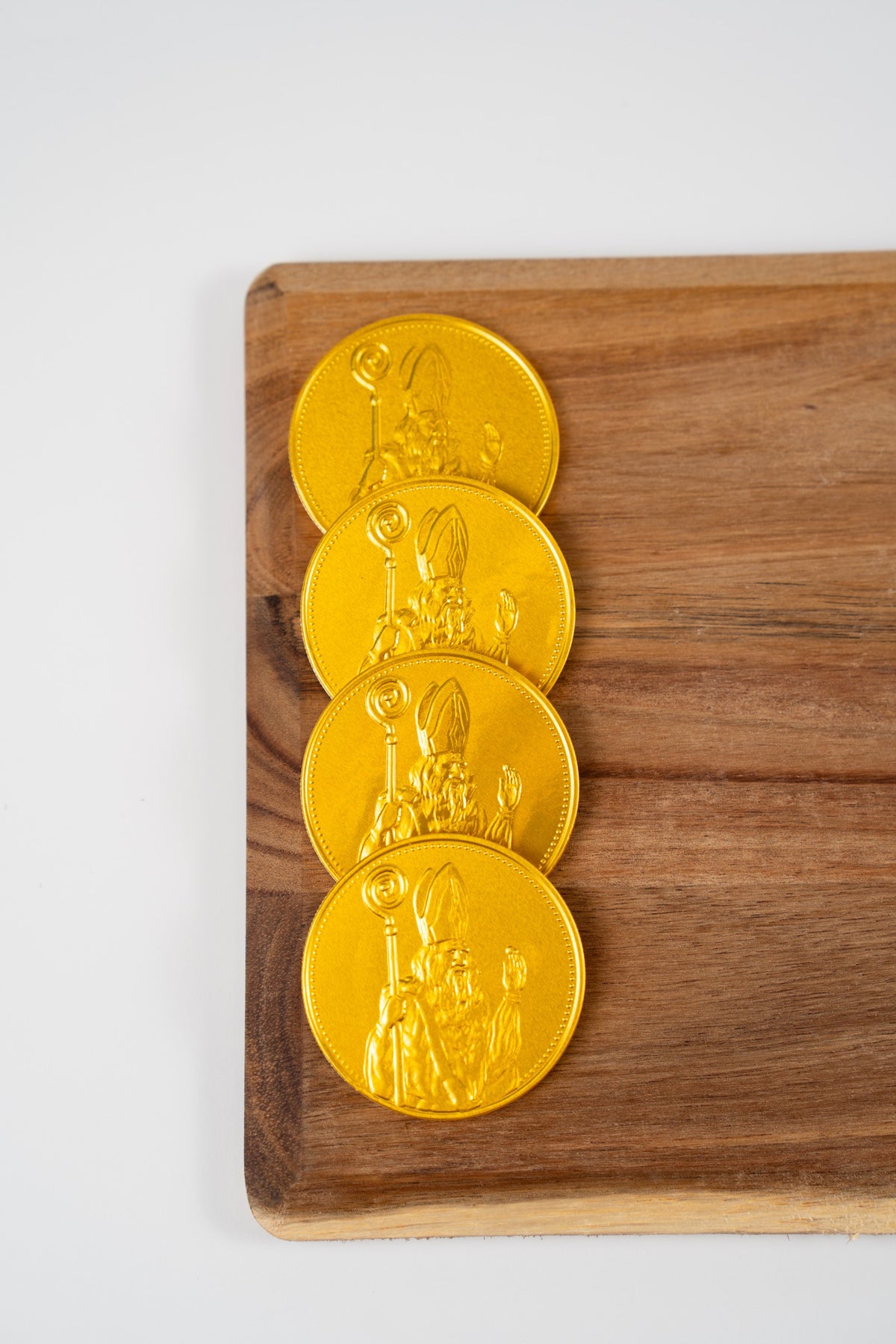 Quatre des cinq médailles Saint-Nicolas en chocolat du coffret, emballées dans une feuille dorée et présentées sur une planche en bois.