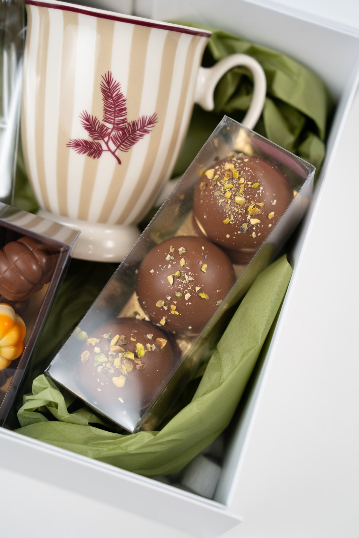 Three Dubai Melocakes in milk chocolate, sprinkled with pistachio pieces and presented in a clear case.