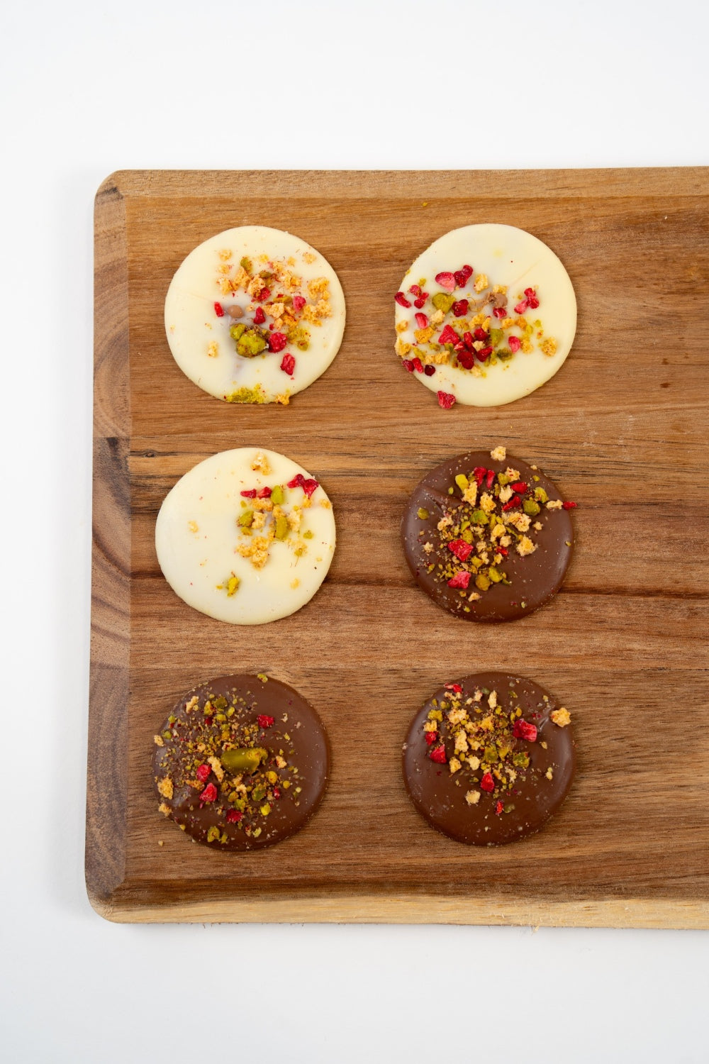 Péché Mignon assortment of Belgian milk and white chocolate mendiants topped with pistachios and freeze-dried raspberry.