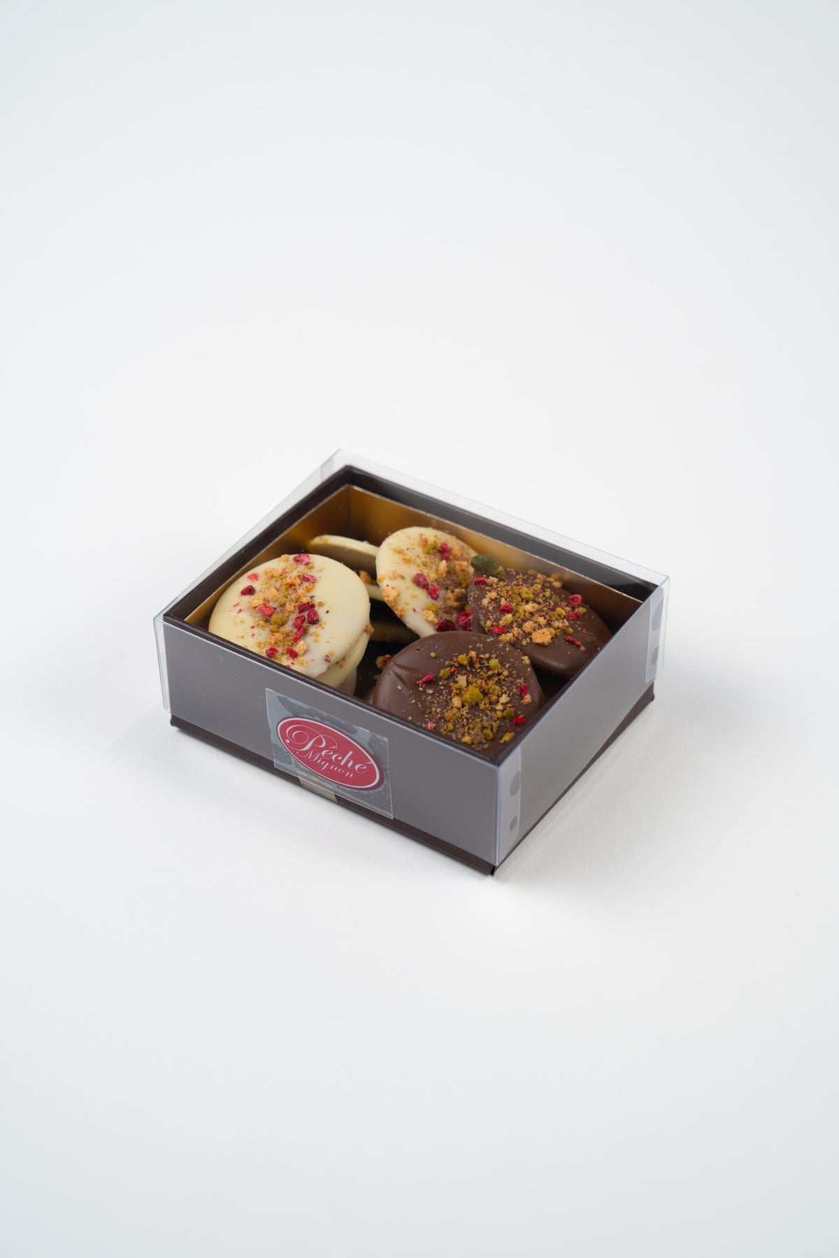 Closed Péché Mignon box containing 150 g of milk and white chocolate mendiants with pistachios and raspberry.