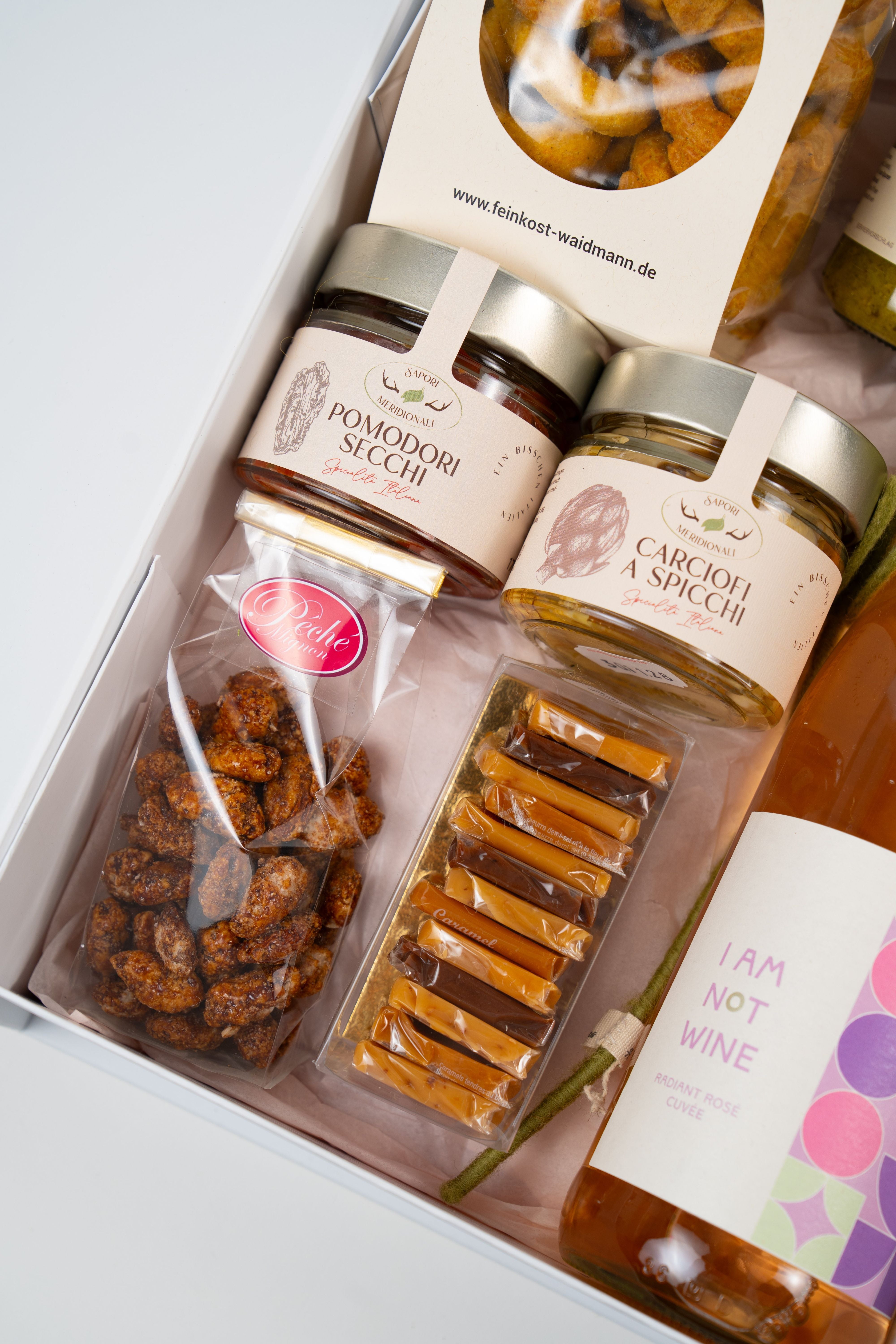 Close-up of Le Péché Mignon gourmet gift box with antipasti jars, caramel candies and roasted nuts
