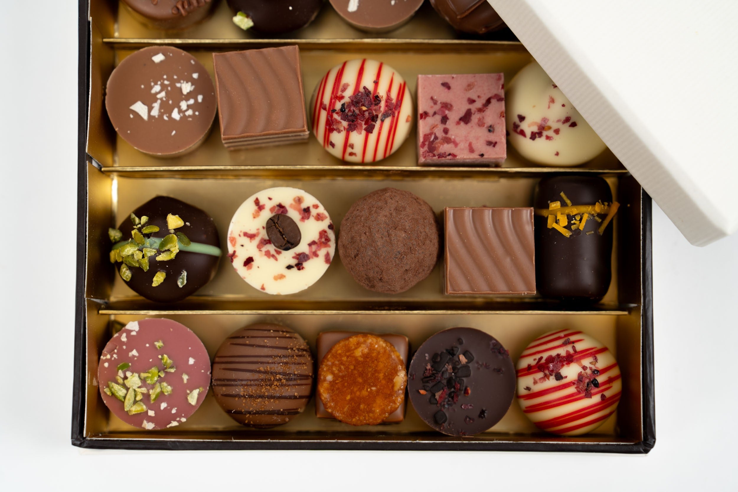 Gros plan sur un coffret de pralines premium avec assortiment de chocolats fins et détails des textures – Péché Mignon
