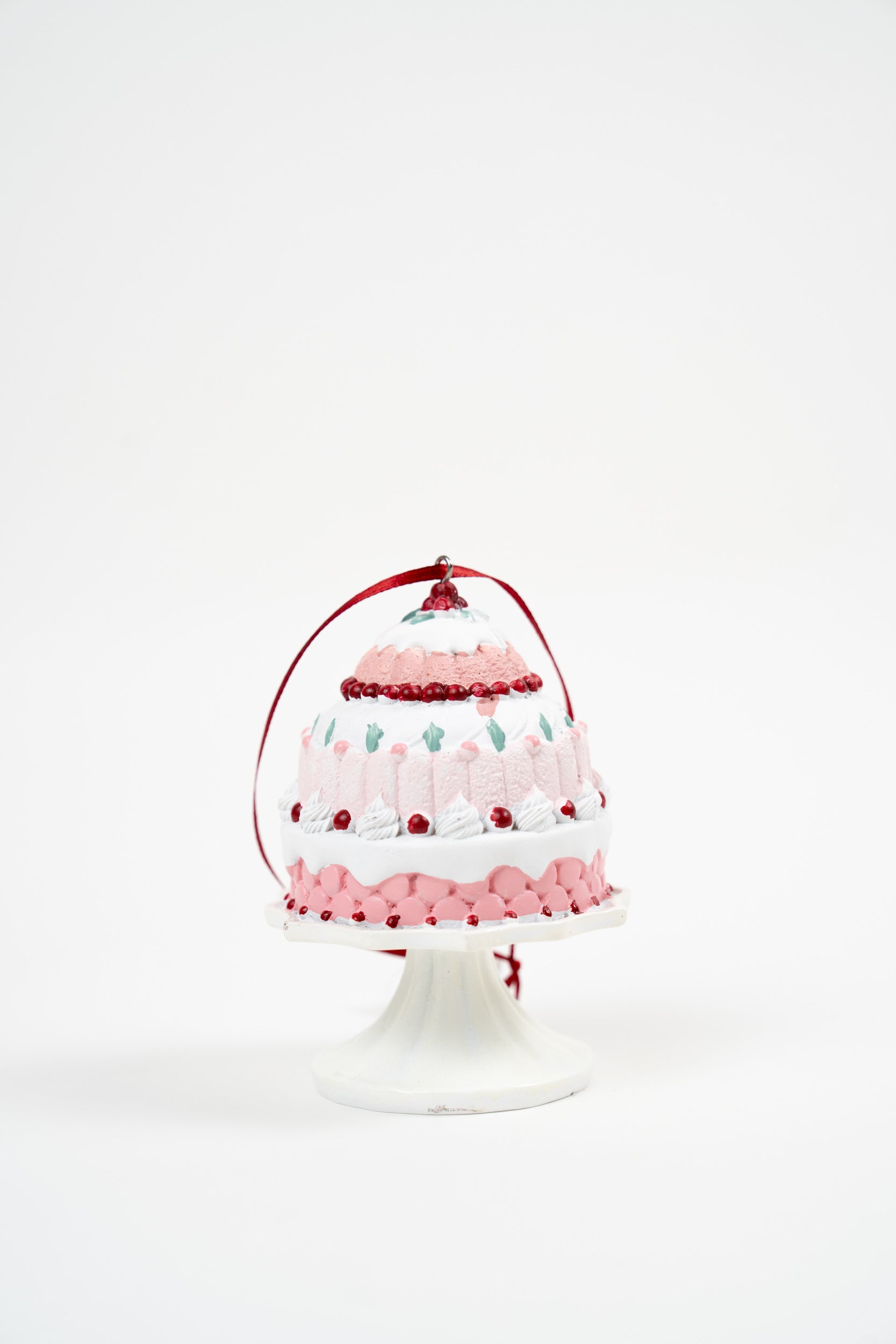 Pink and white tiered cake ornament on a pedestal stand with red ribbon hanging loop.