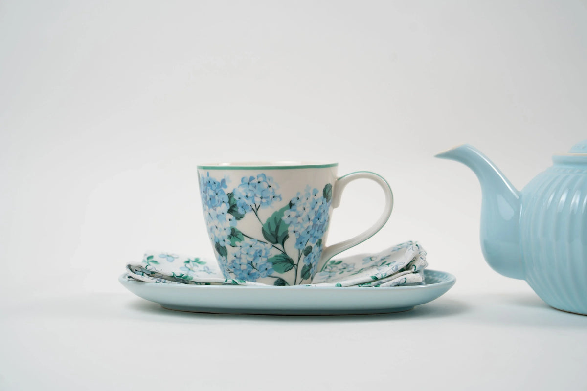 Tasse en porcelaine ornée de motifs floraux bleus, présentée avec sa soucoupe et sa serviette assortie. Un ensemble délicat pour une ambiance élégante et poétique.