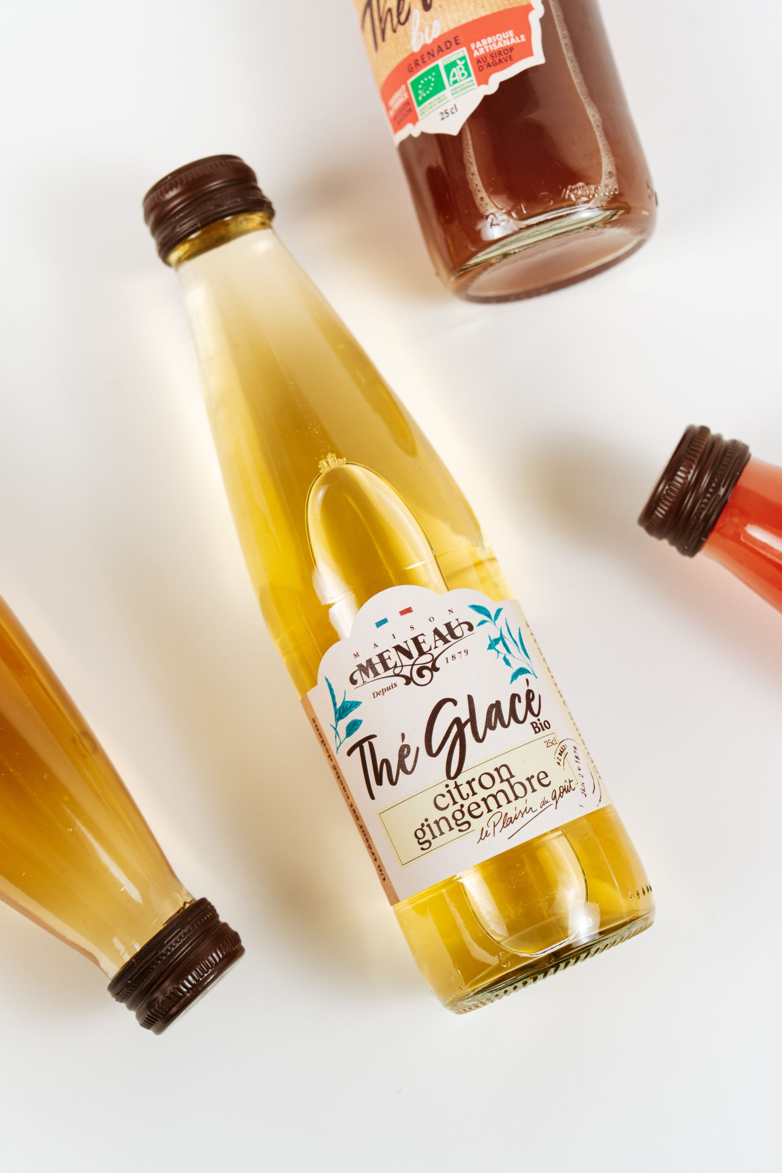 Bouteille de thé glacé bio citron gingembre Maison Meneau avec boissons en arrière-plan.