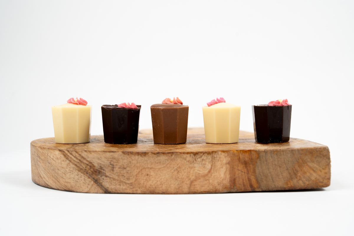 Assorted luxury chocolates with floral decoration in milk, dark and white chocolate displayed on wooden board