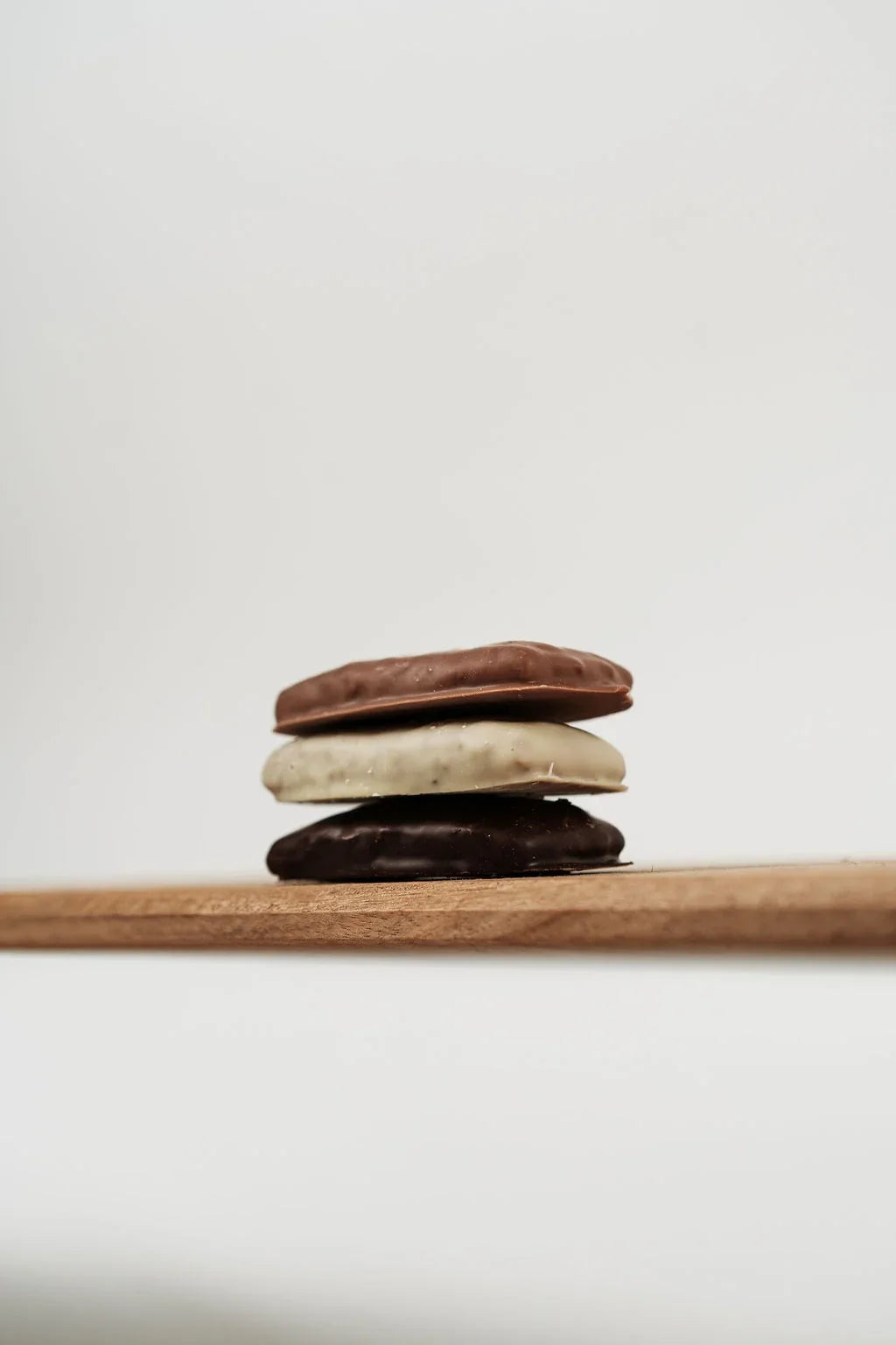 Drie Weichprinten met pure, melk- en witte chocolade, gestapeld op een houten plank.