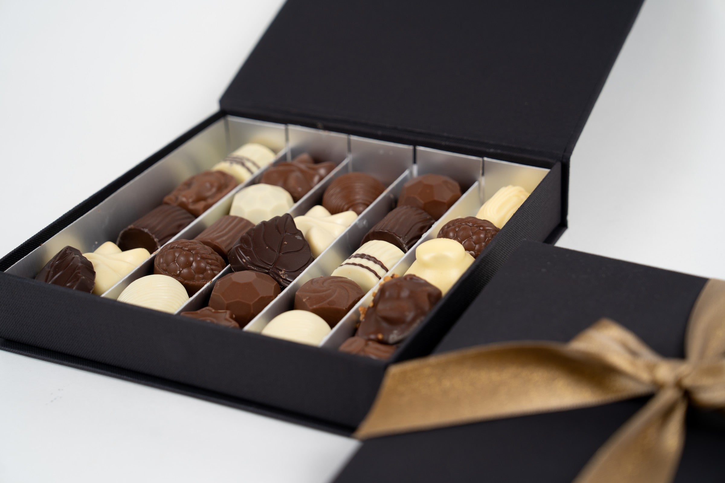 Assortiment de pralines artisanales belges jaunes, vertes et roses dans un coffret doré Péché Mignon