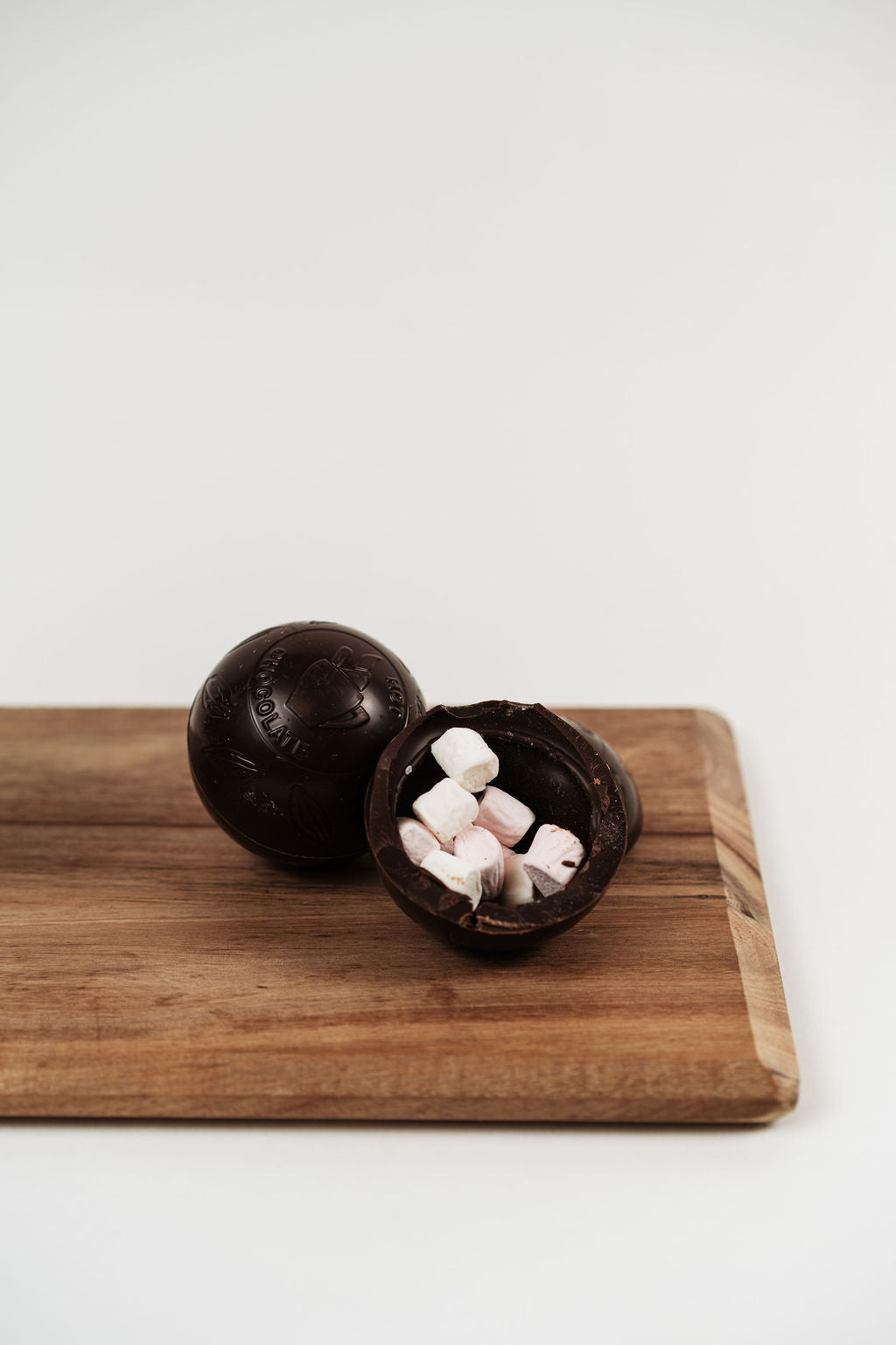 Bombe de chocolat chaud noir ouverte avec mini marshmallows à l’intérieur sur planche en bois