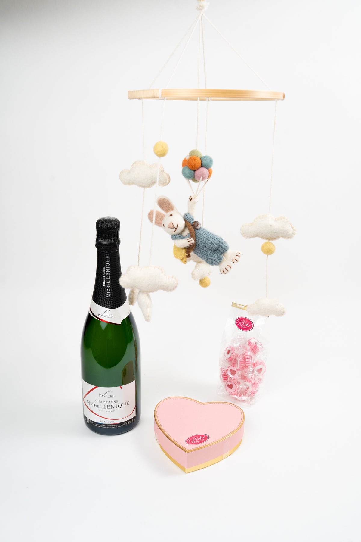 Luxury champagne and chocolate gift set with heart-shaped box, sweets and decorative baby mobile styling.