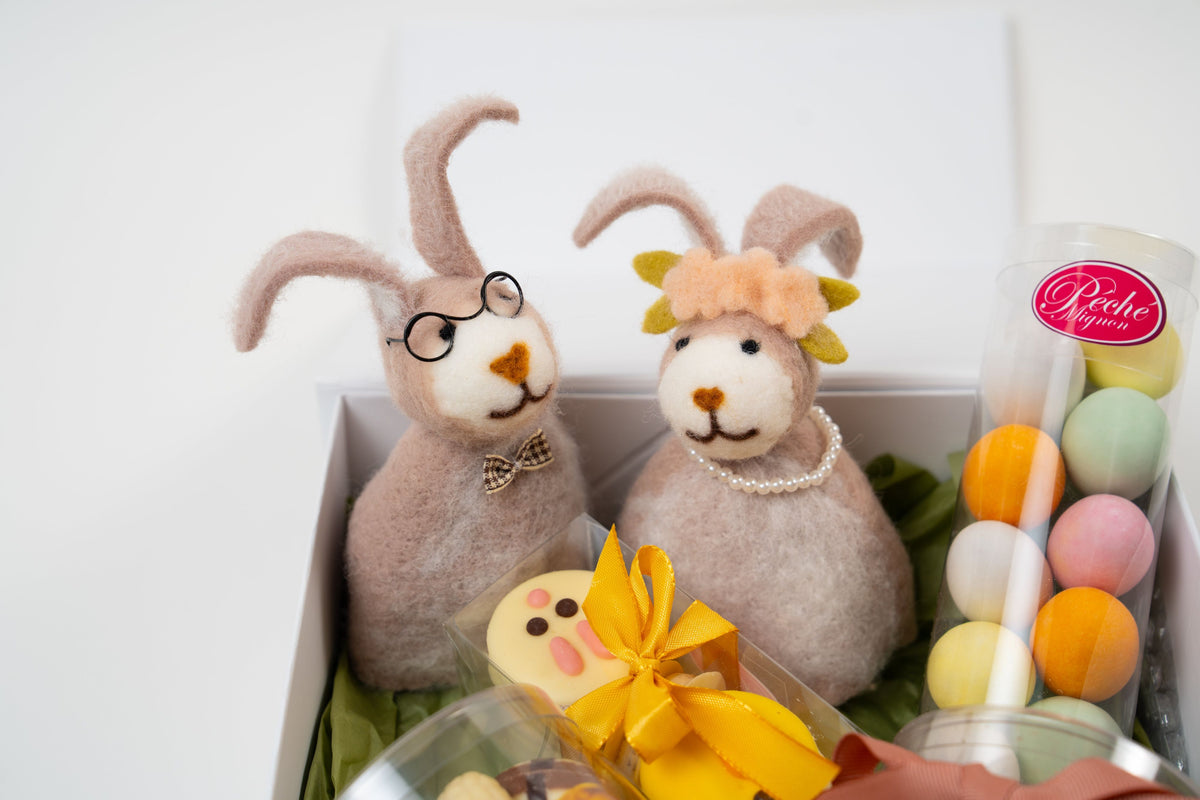 Deux chauffe-œufs en feutrine artisanale en forme de lapins gris et blanc accompagnés de macarons décorés, décoration de table Univers de Pâques.