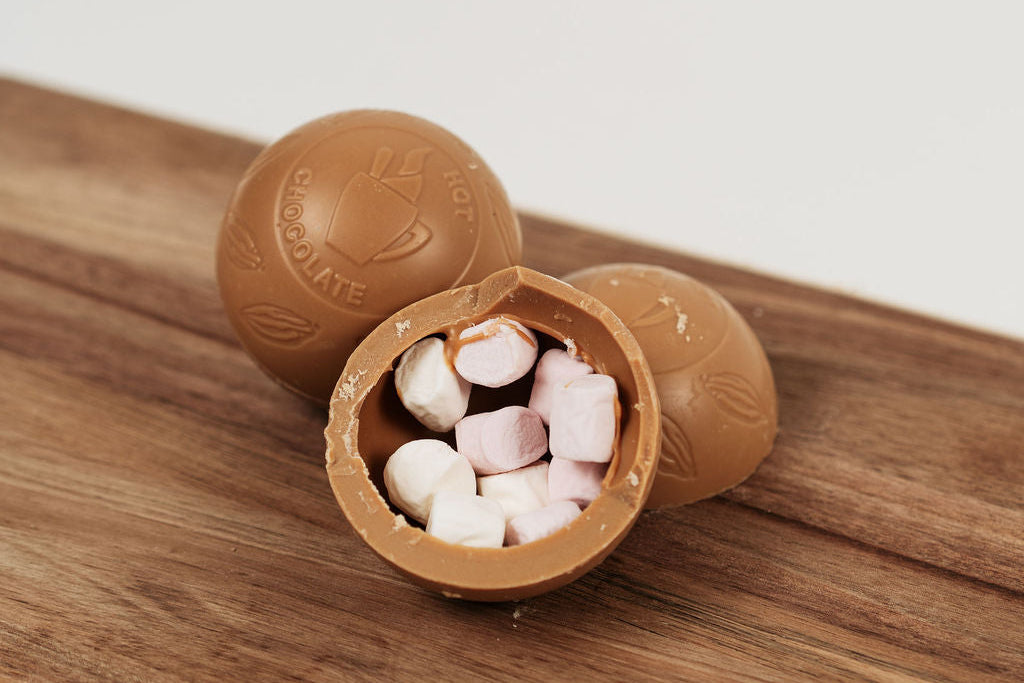 Bombe de chocolat chaud garnie de marshmallows fondants, ouverte sur planche en bois