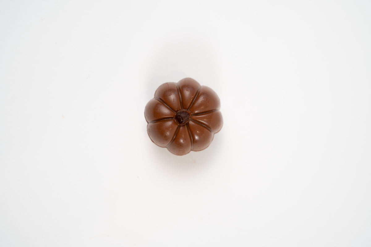 Citrouille en chocolat au lait belge fourrée au caramel au beurre, présentée seule sur fond blanc.