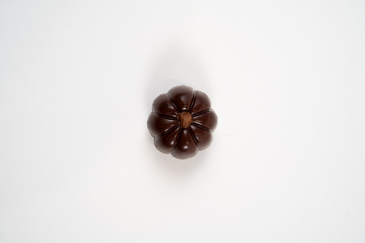 Citrouille en chocolat noir belge fourrée à la crème de framboise, présentée seule sur fond blanc.