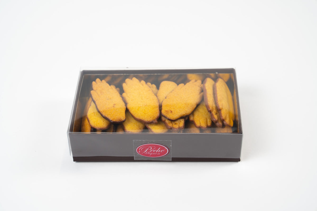 Vooraanzicht van een Péché Mignon-geschenkdoos met goudkleurige handvormige koekjes met chocoladerand, onder een transparant deksel op een witte achtergrond.
