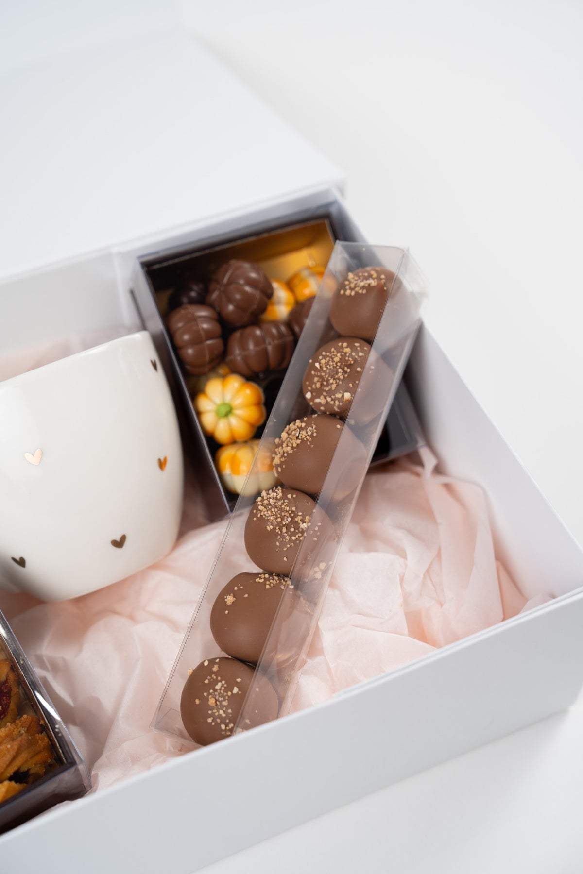 Close-up of six milk-chocolate Mini Melocakes with sprinkles, pumpkin chocolates and a white mug
