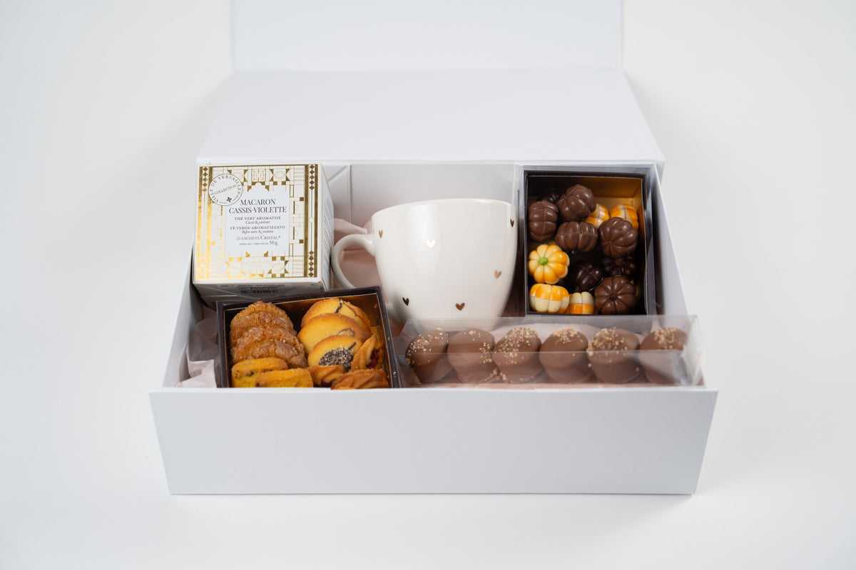 Front view of an open white autumn gift box with tea, mug, biscuits, pumpkin chocolates and six Mini Melocakes