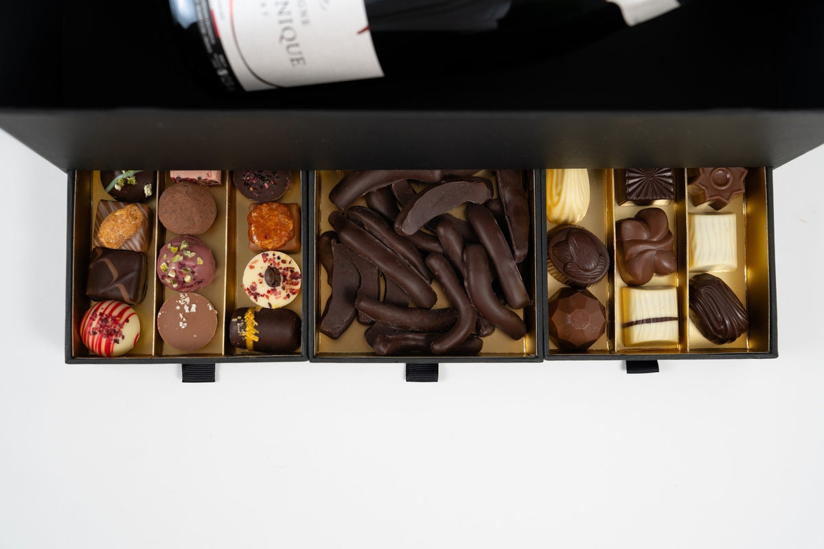 Vue de dessus des trois tiroirs de pralines et d’orangettes, avec la bouteille de Champagne dans le coffret