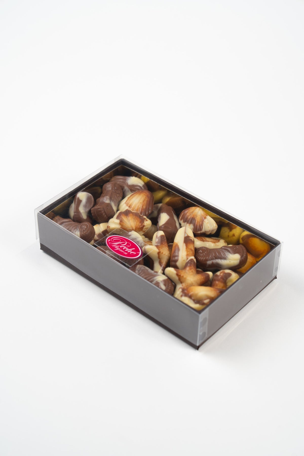 Péché Mignon box of Belgian marbled milk and white chocolate seashells and sea creatures, with a clear lid on a white background.