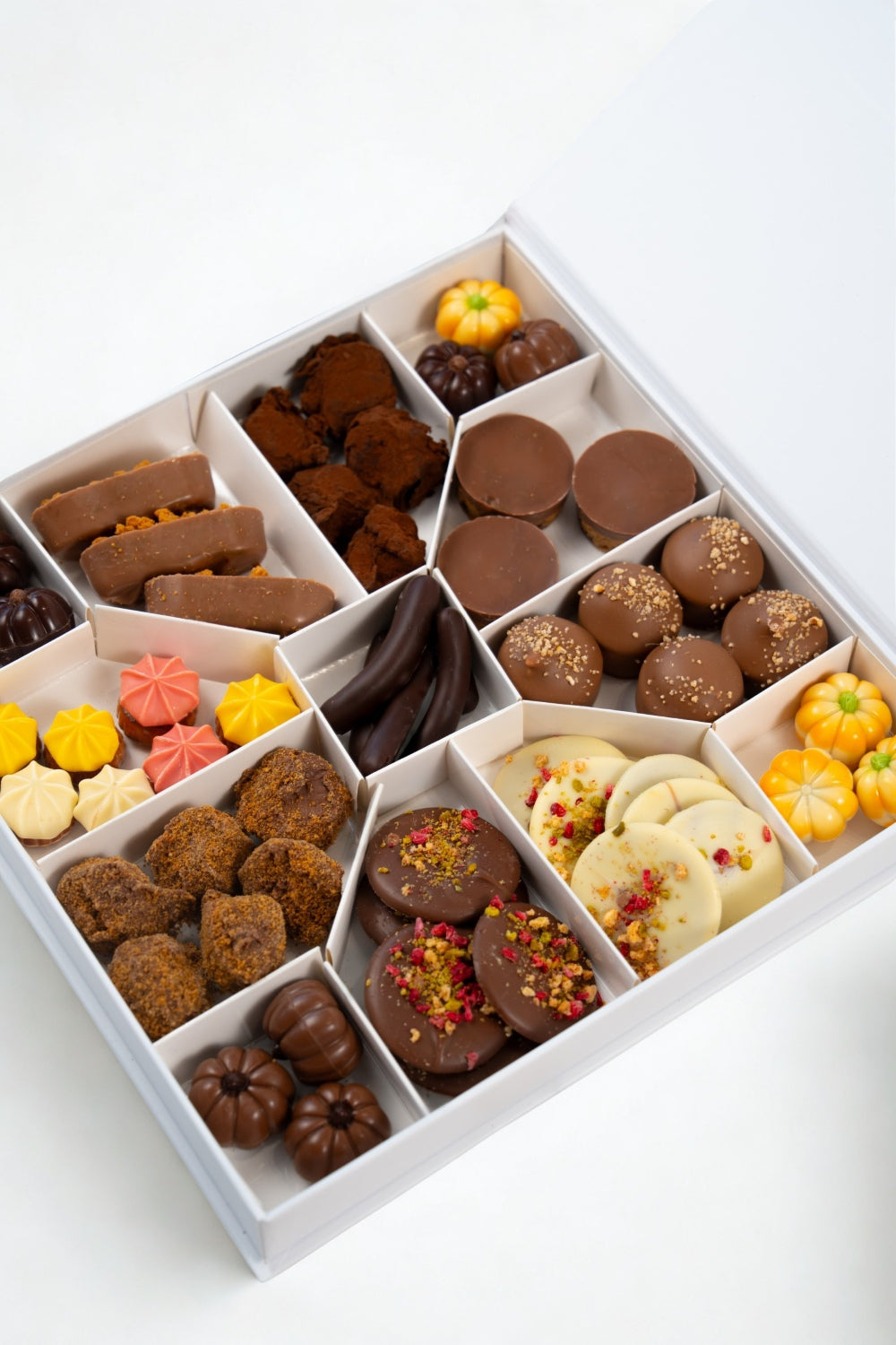 Open Péché Mignon autumn gift box with assorted chocolates, truffles, mendiants, bites and pumpkin-shaped chocolates arranged in white compartments.