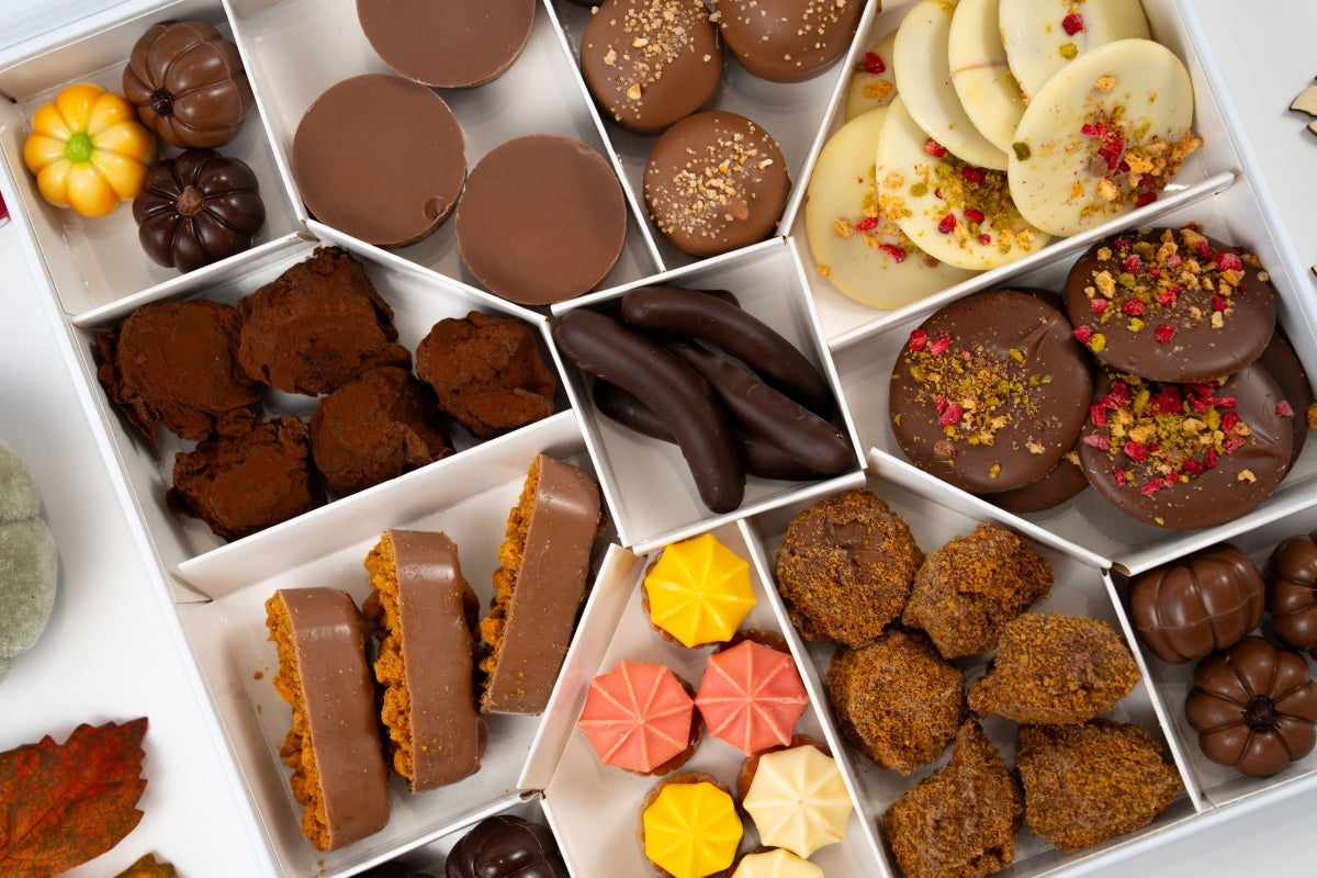 Top view of a compartmented autumn gift box with truffles, chocolate bites, milk and white chocolate mendiants, colourful sweets and pumpkin-shaped chocolates.