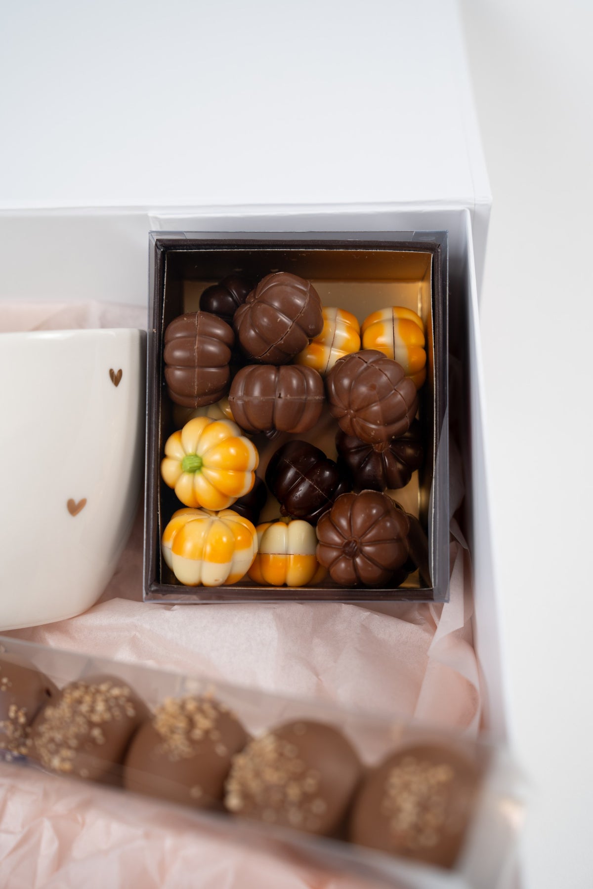 Assorted milk, white, orange and dark chocolate pumpkins in a rectangular box with a gold interior