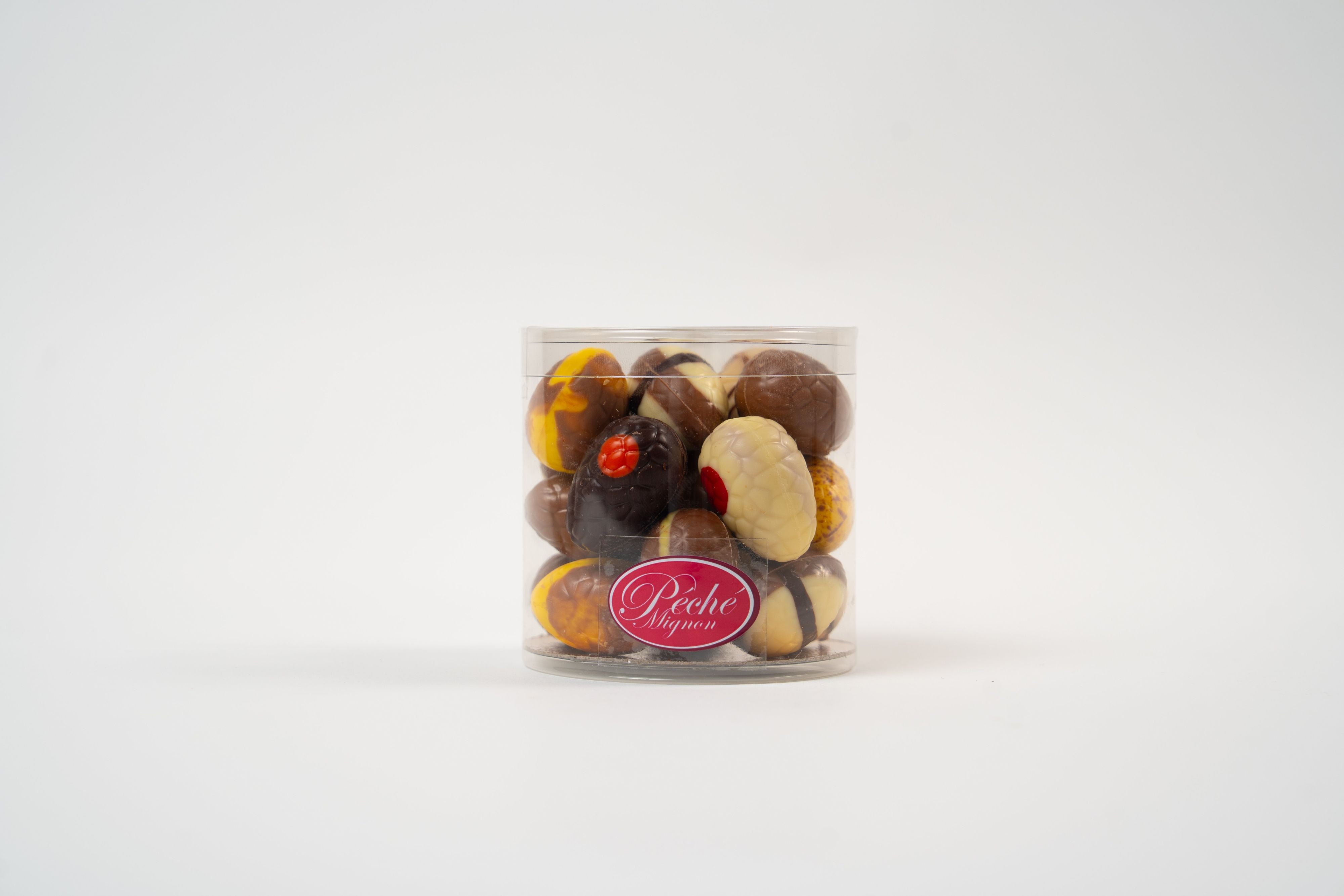 Coffret cadeau transparent d'œufs gourmands en chocolat Péché Mignon, assortiment de chocolats fourrés artisanaux pour offrir lors des fêtes de Pâques.