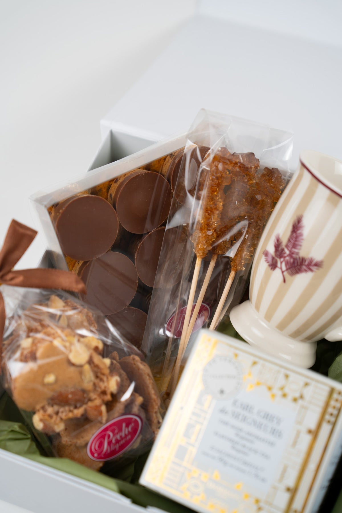 Close-up of round milk chocolates, almond meringues and three brown rock sugar sticks in a white gourmet gift box.