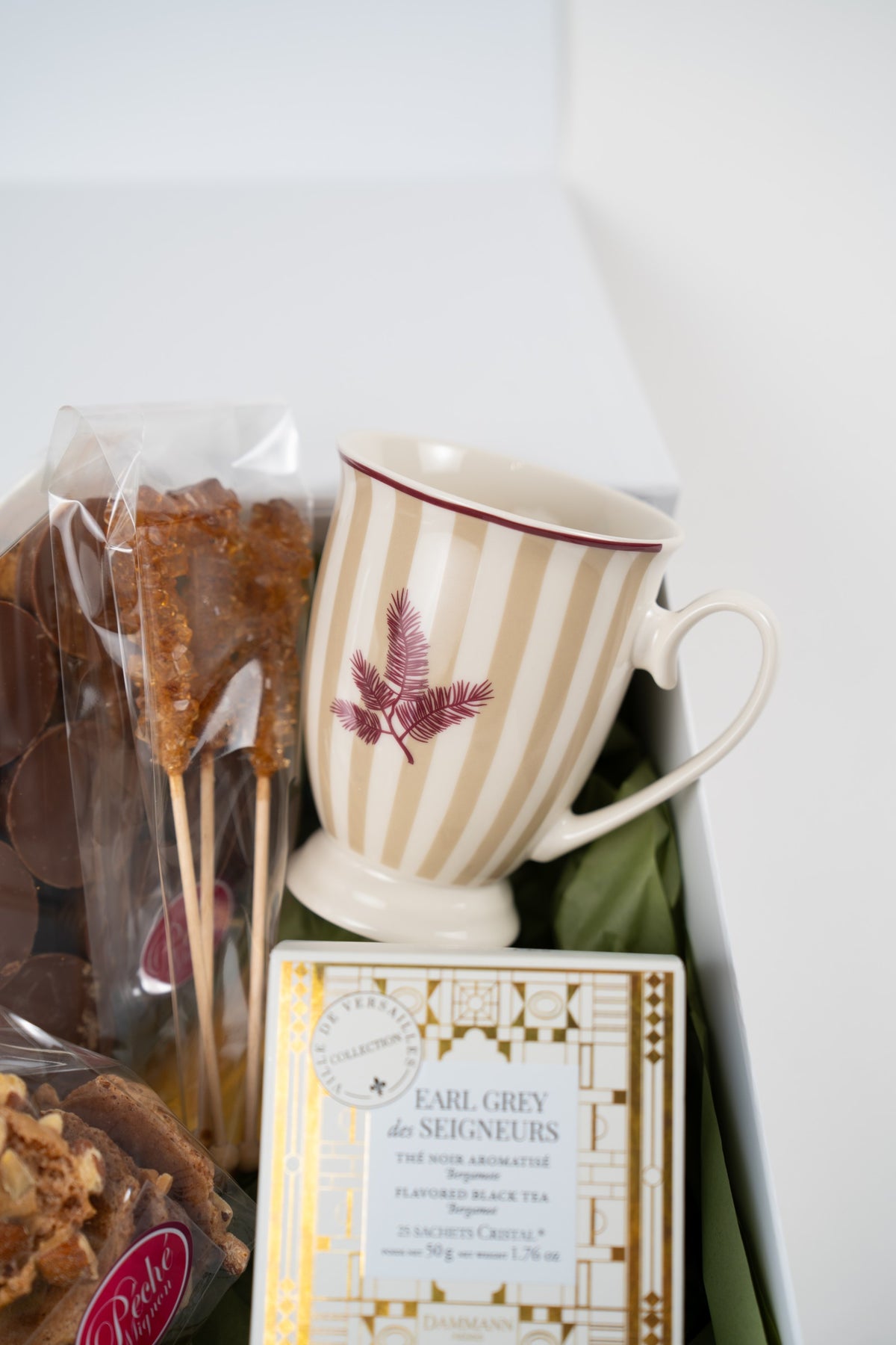 Beige-striped ceramic mug with burgundy botanical detail, three brown rock sugar sticks and Earl Grey tea in a gift box.