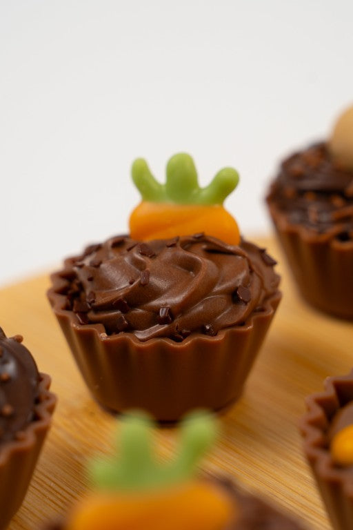 Gros plan sur un cupcake artisanal en chocolat en forme de carotte. Détails du glaçage orange et de la base en chocolat belge, décoré d'une crème crispy. Confiserie de Pâques Péché Mignon.