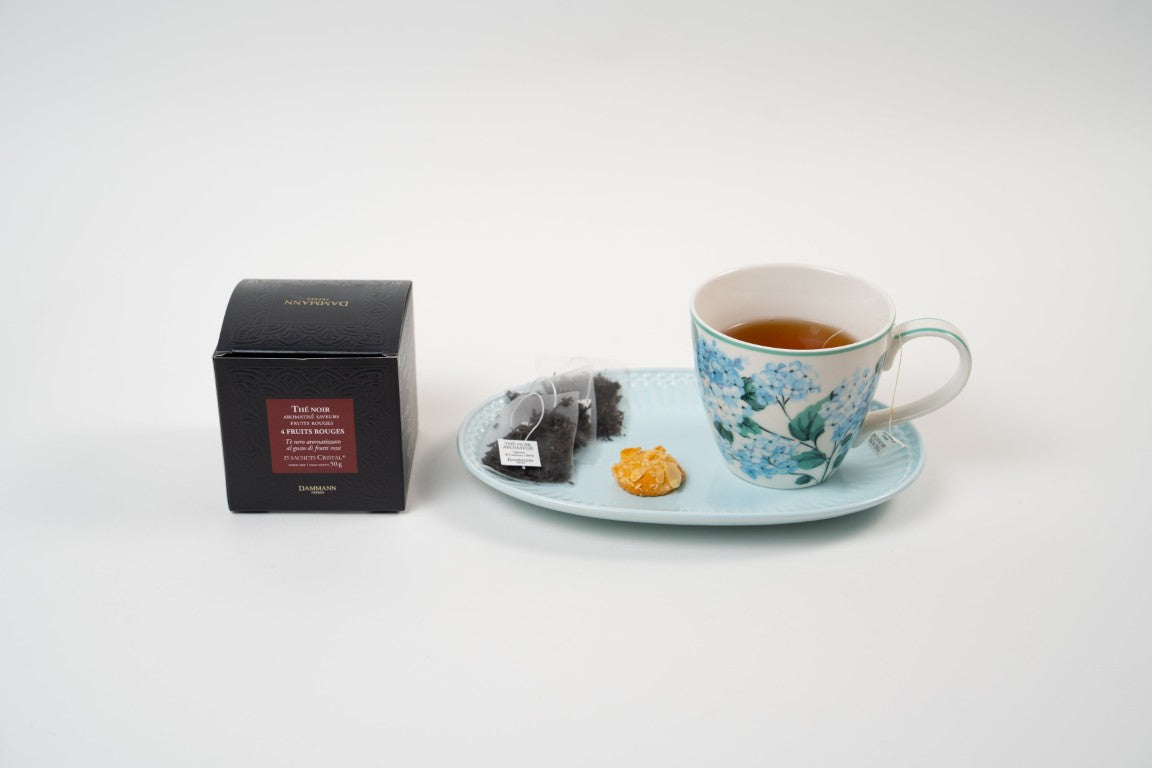 Dammann Frères 4 Fruits Rouges black tea with teacup, tea sachets and biscuit on blue plate.