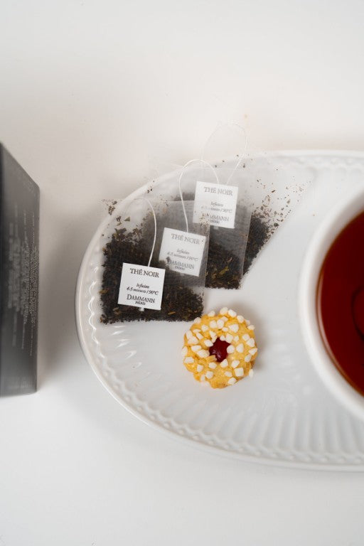 Dammann Frères Breakfast black tea sachets with cup of tea and biscuit on white plate.