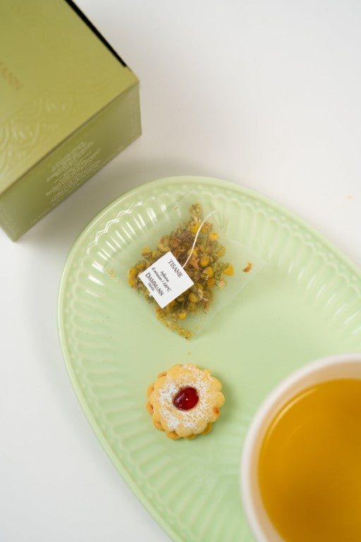 Chamomile herbal tea with tea bag, biscuit and Dammann Frères chamomile infusion tea box on plate.